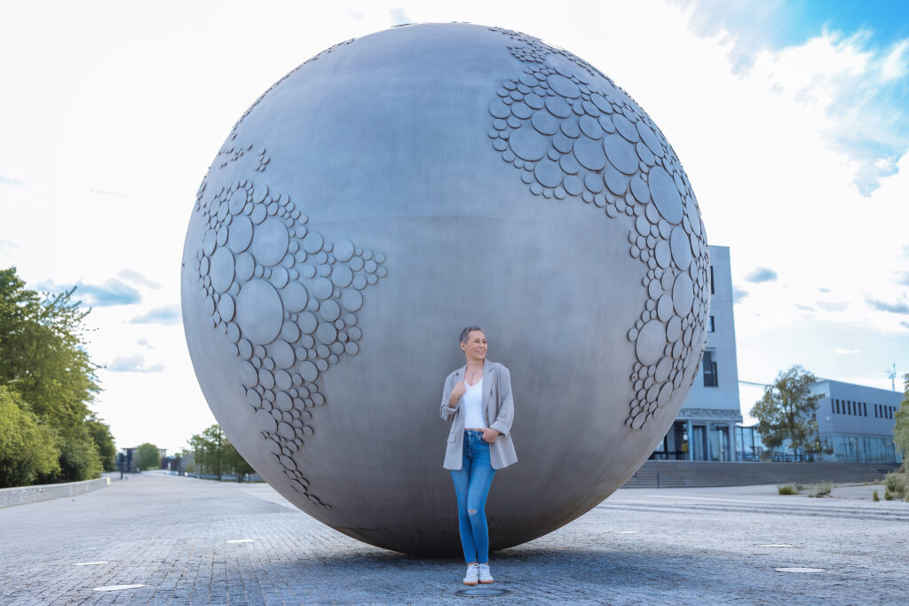 Woman stands beside large gray globe sculpture with circular indentations