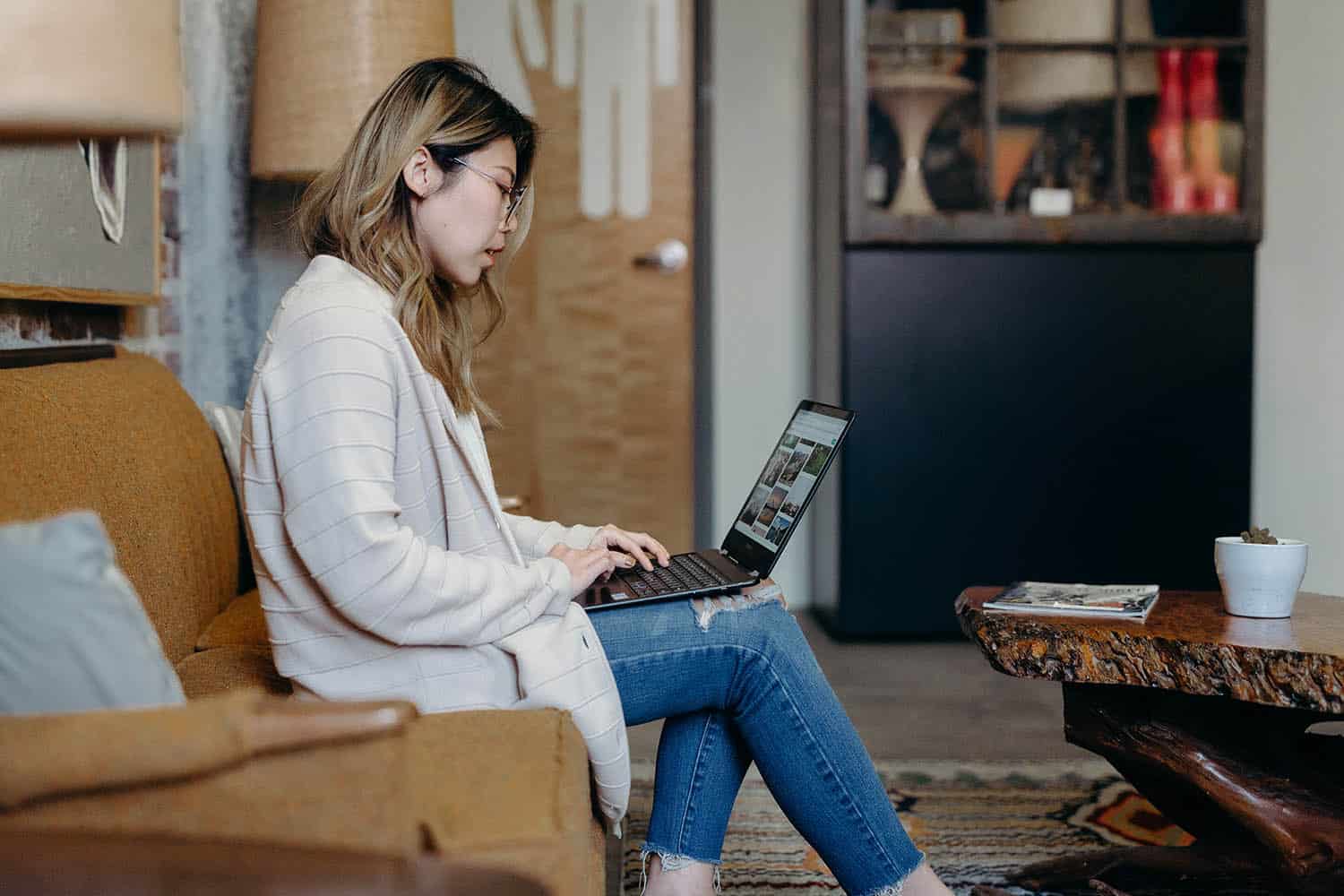 A photographer edits photos in Lightroom while sitting on a vintage sofa
