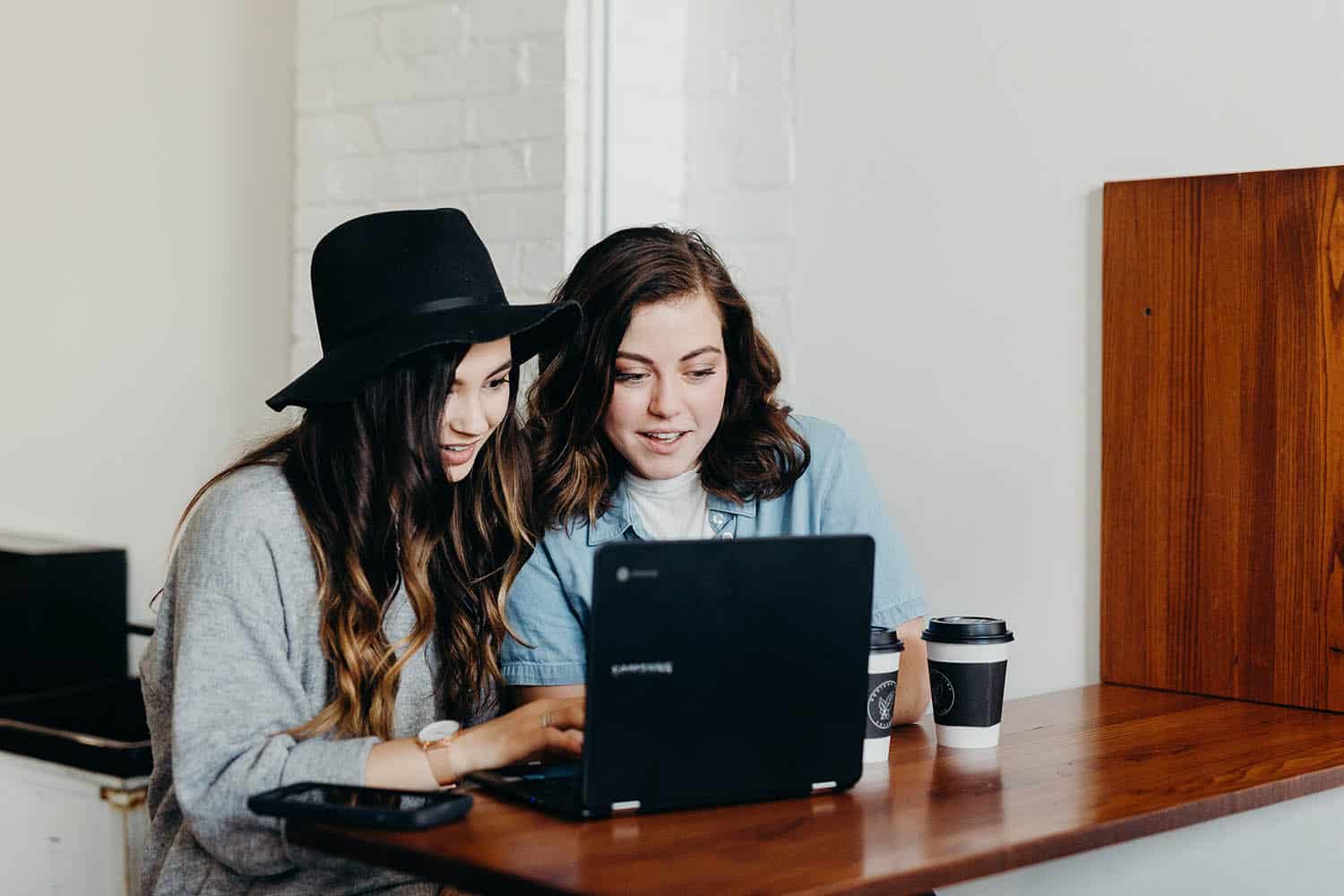 Two photographers sit at a table looking at batch edited photos in Lighroom on their laptop
