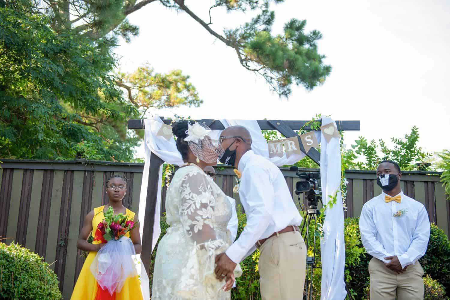 A bride and groom share their first kiss as husband and wife in front of their mask-wearing guests during COVID-19