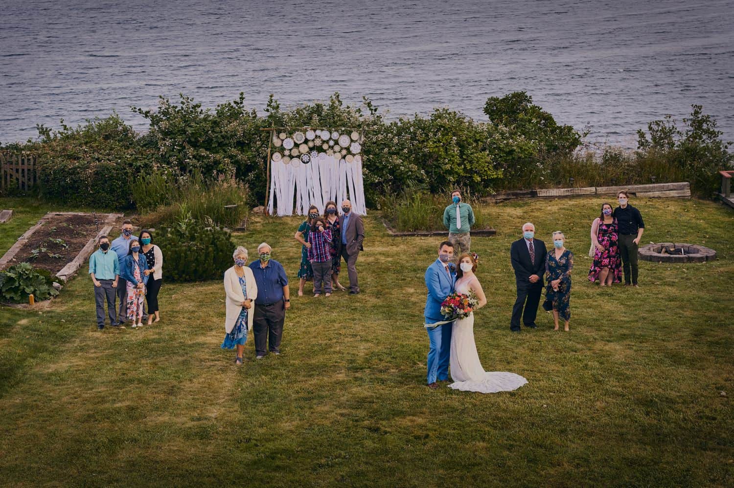A socially distanced family portrait in a large seaside field after an outdoor wedding during COVID-19
