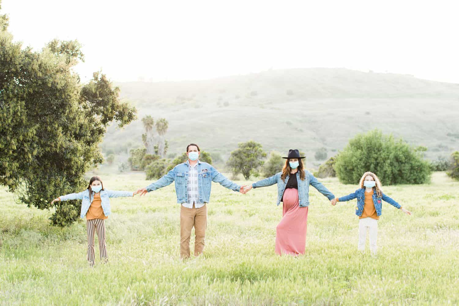 A family stands at a social distance in a field while holding hands and wearing masks during the COVID-19 pandemic