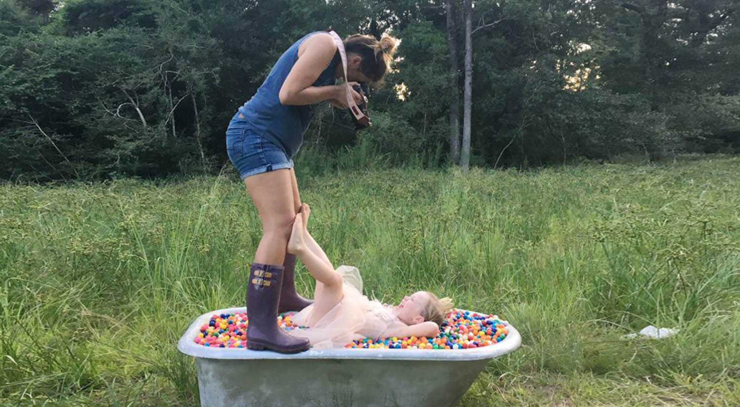 Photographer Shalonda Chaddock stands over a clawfoot tub during an outdoor photo shoot with a young child