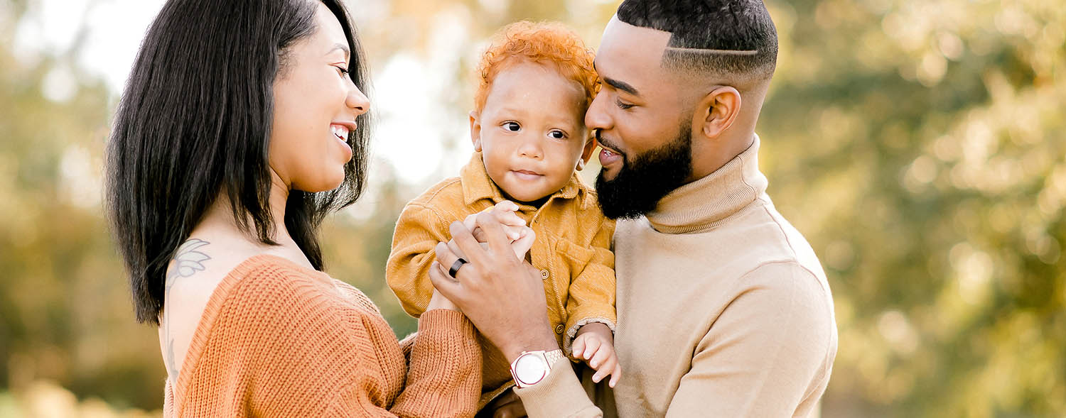 A mom, dad, and toddler son snuggle close together in a vibrant outdoor portrait