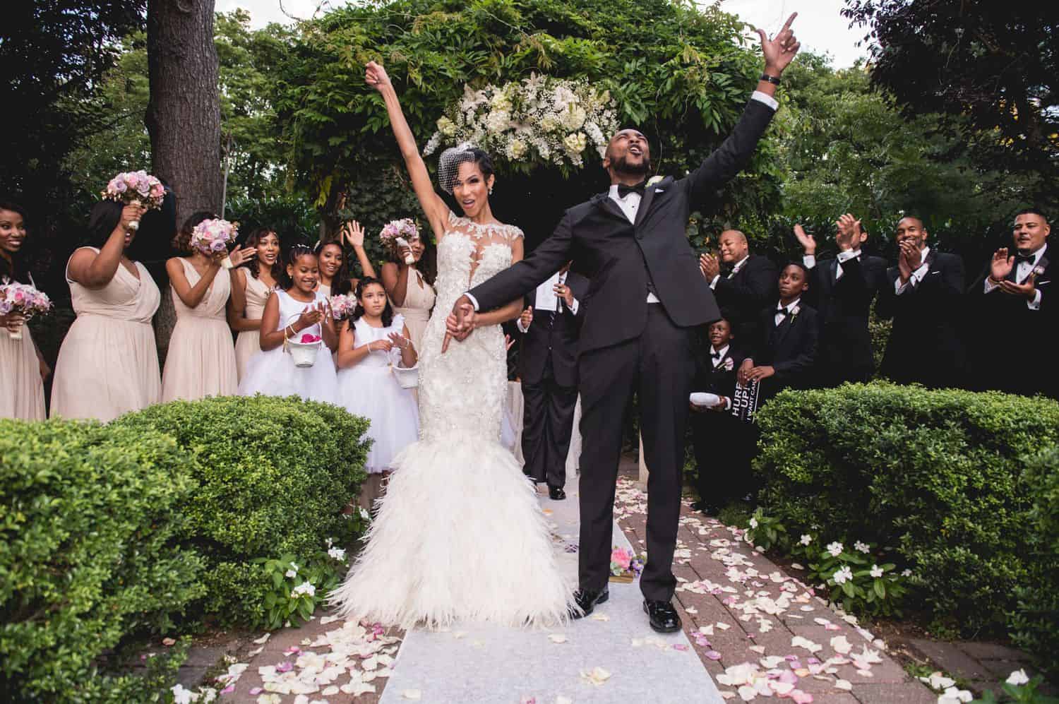 A newlywed couple cheering with their hands up as they walk down the aisle
