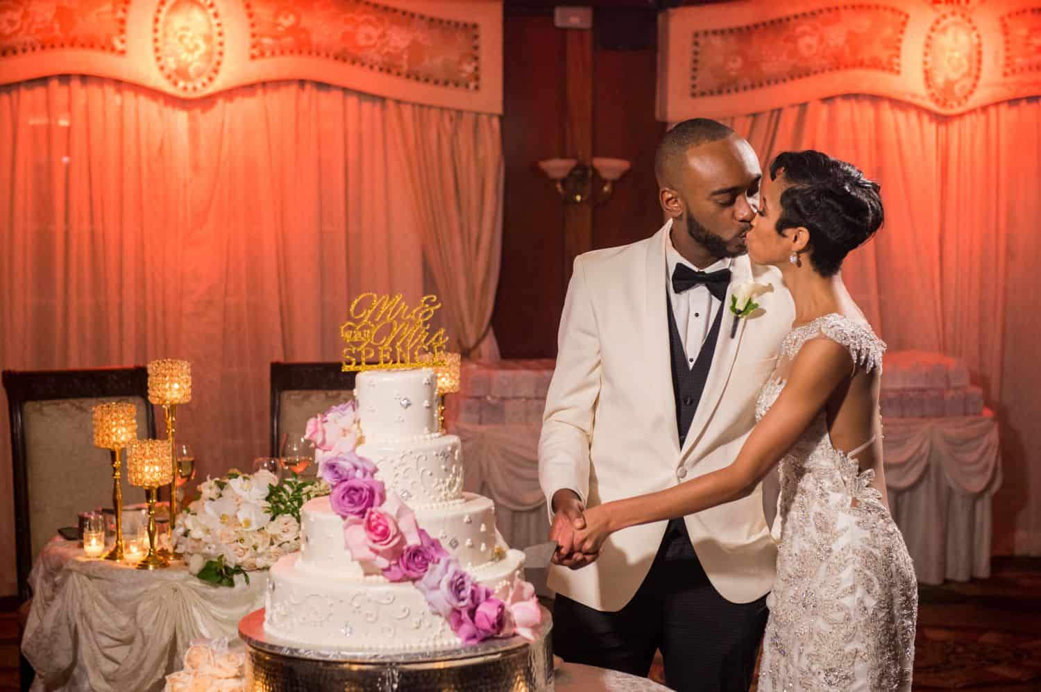 A newlywed couple cutting the cake while kissing