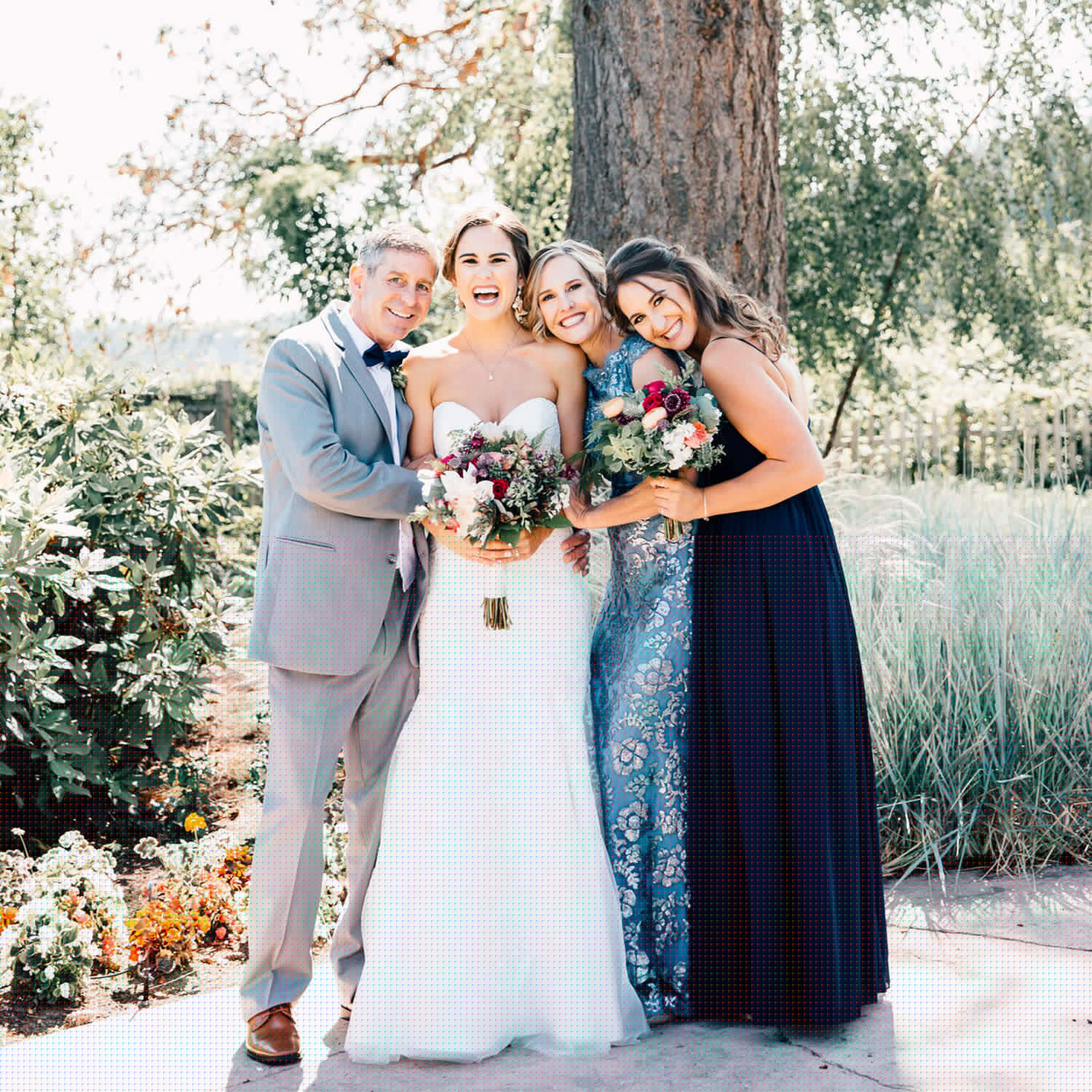 A bride poses outside with her mom, dad, and sister