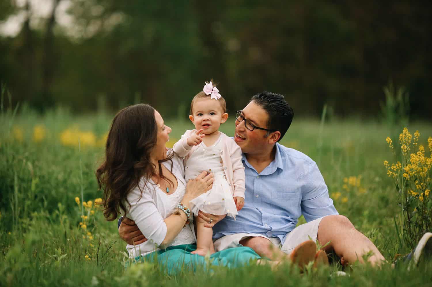 Two parents sit in a field on either side of their tiny daughter