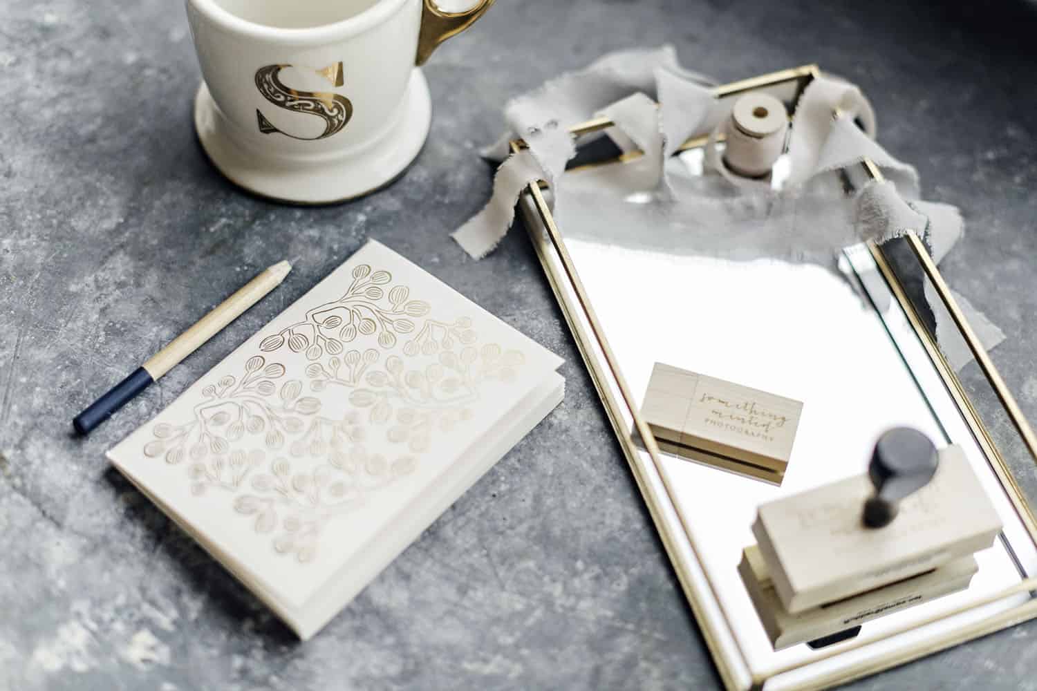 A gray marbled workspace is laid out with a journal, coffee mug, and other desk accessories