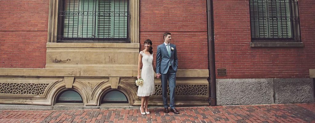 a1 bride and groom hold hands by brick wall