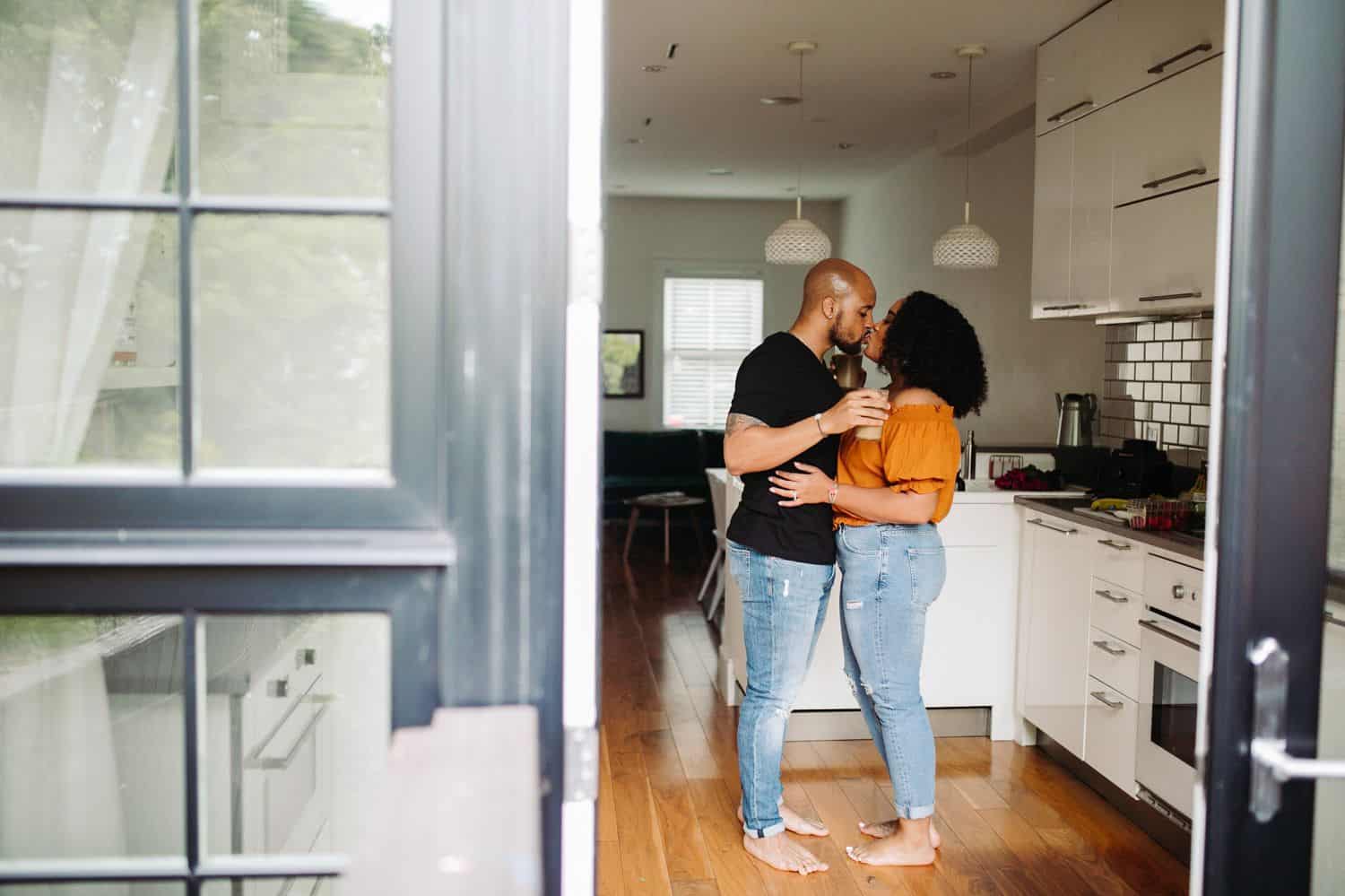 A Black couple stands in the kitchen of their Atlanta Airbnb where they've hired Kiyah C. to make their portraits