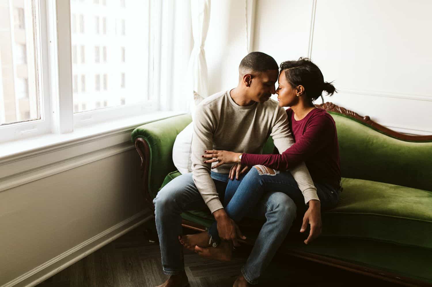A Black couple snuggles on the vintage green sofa in their Atlanta Airbnb
