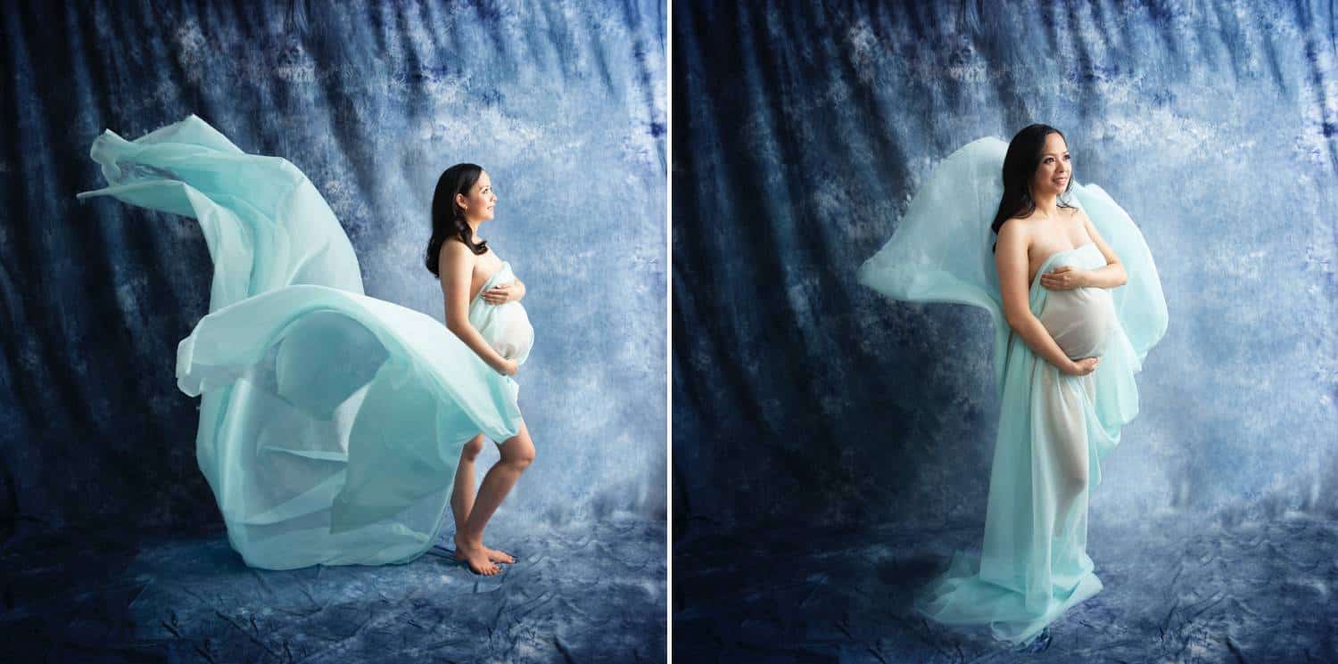 A pregnant woman is photographed against a deep blue studio backdrop. A light teal gown swirls around her.