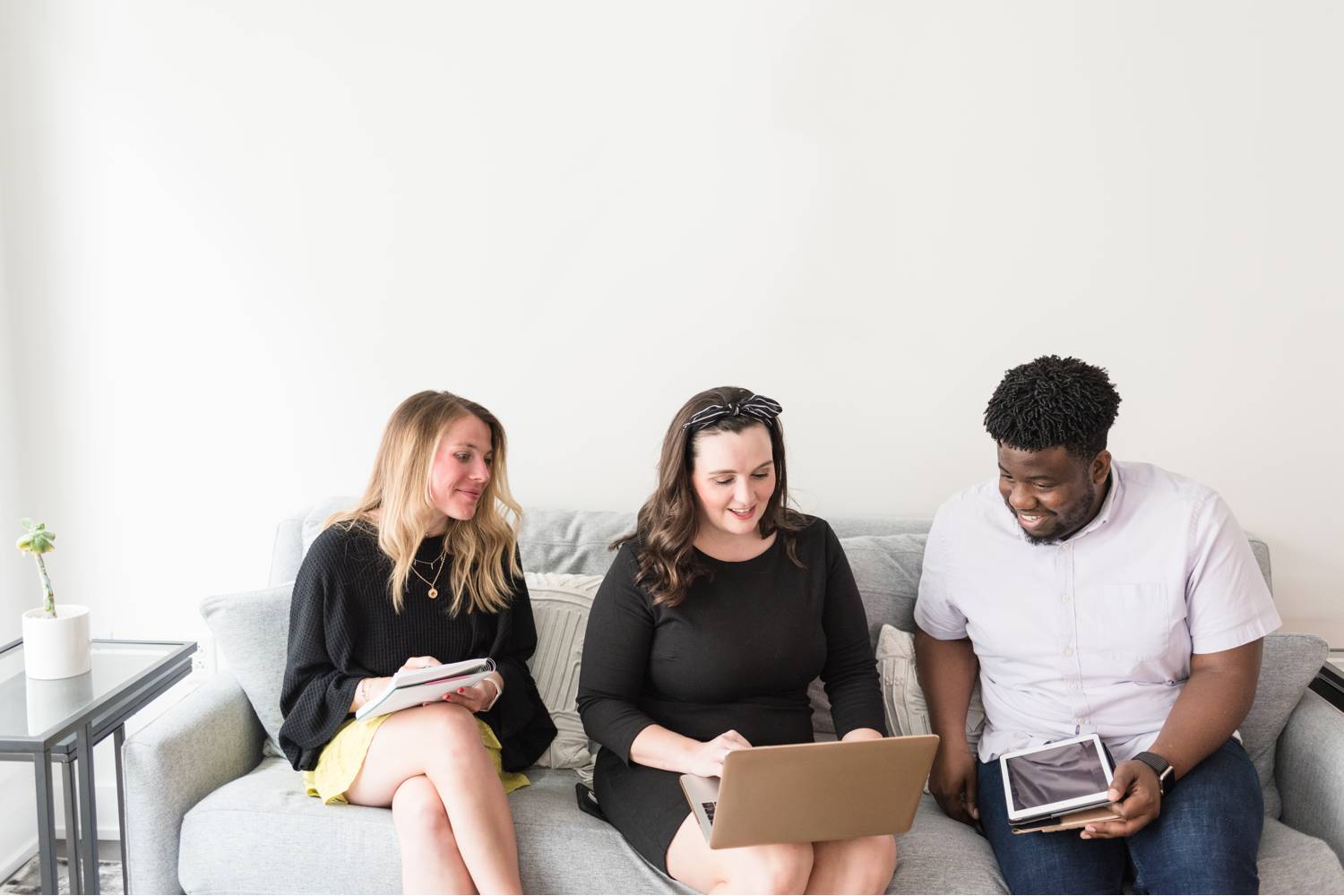 By Mandy Liz: Three adults sit on a sofa smiling and reviewing client feedback on a laptop.
