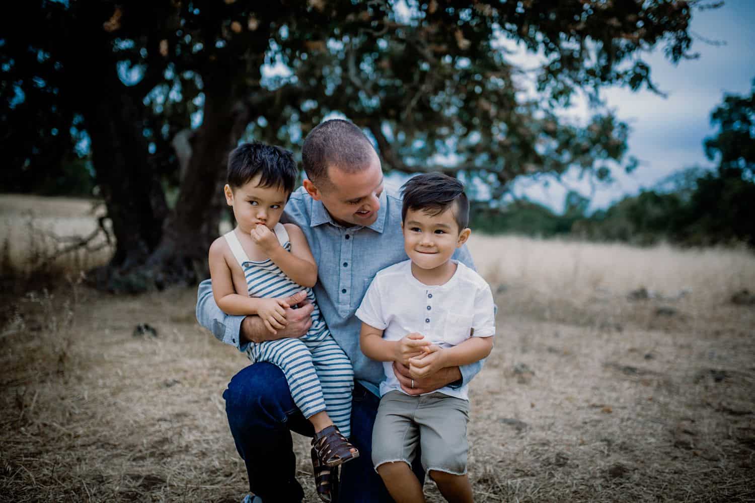 A father kneels in a field holding his two sons on his knees.