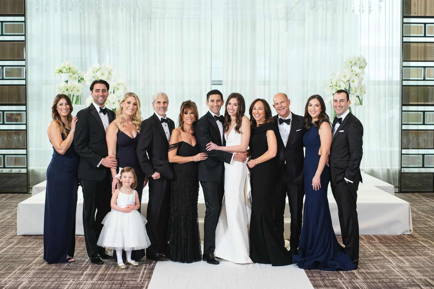 A large family poses in front of a white drape for a wedding day portrait