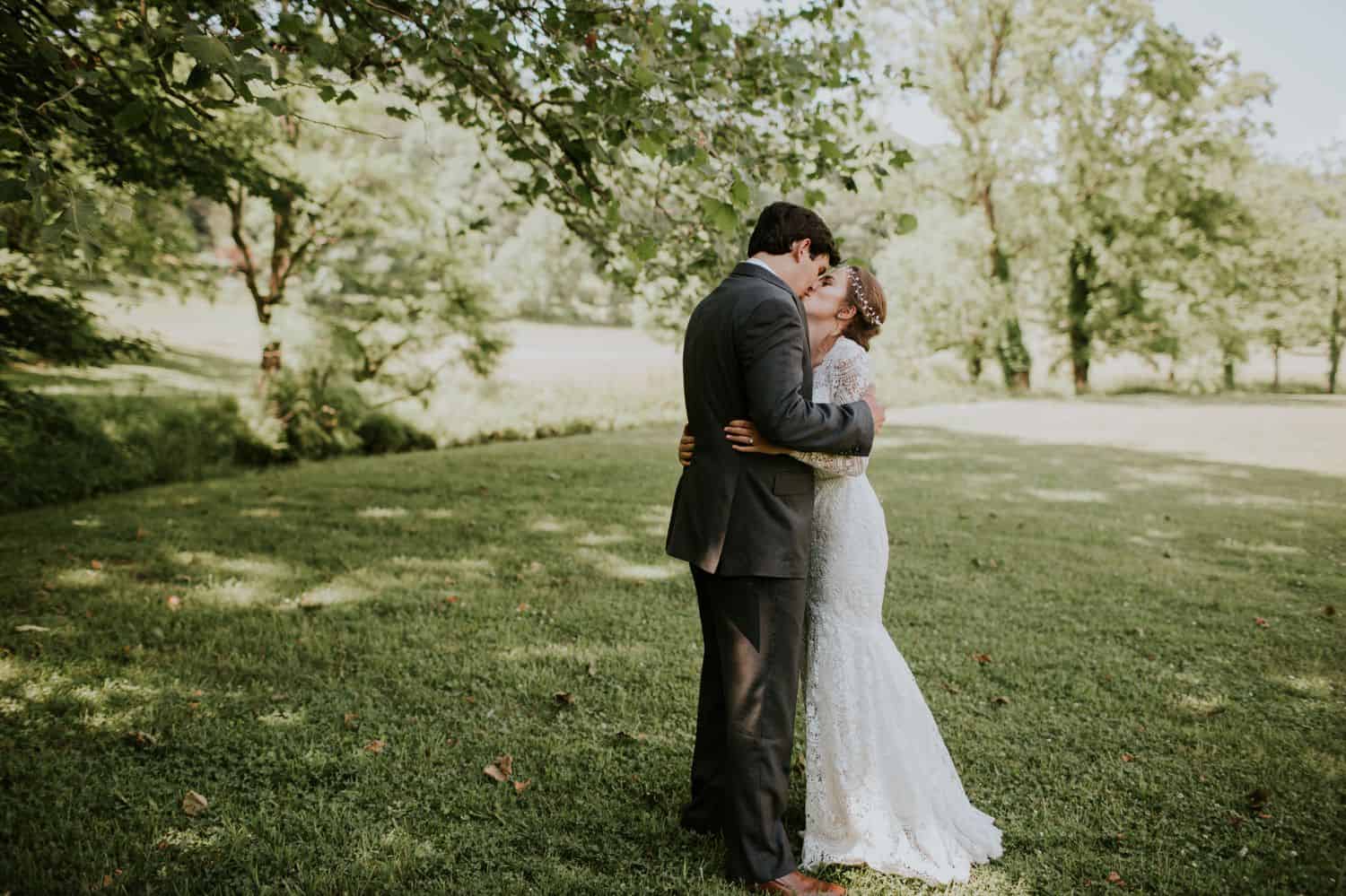 A bride and groom kiss while standing under a tree for their first look on their wedding day.