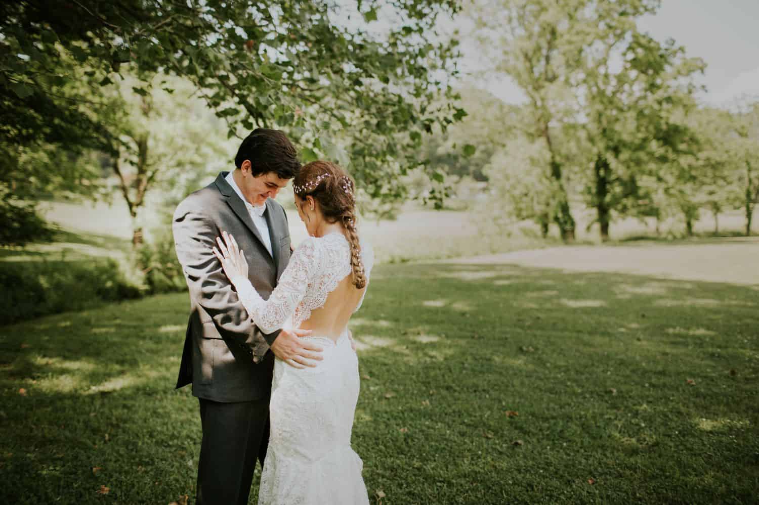 A bride and groom stand forehead-to-forehead under a tree for their first look.