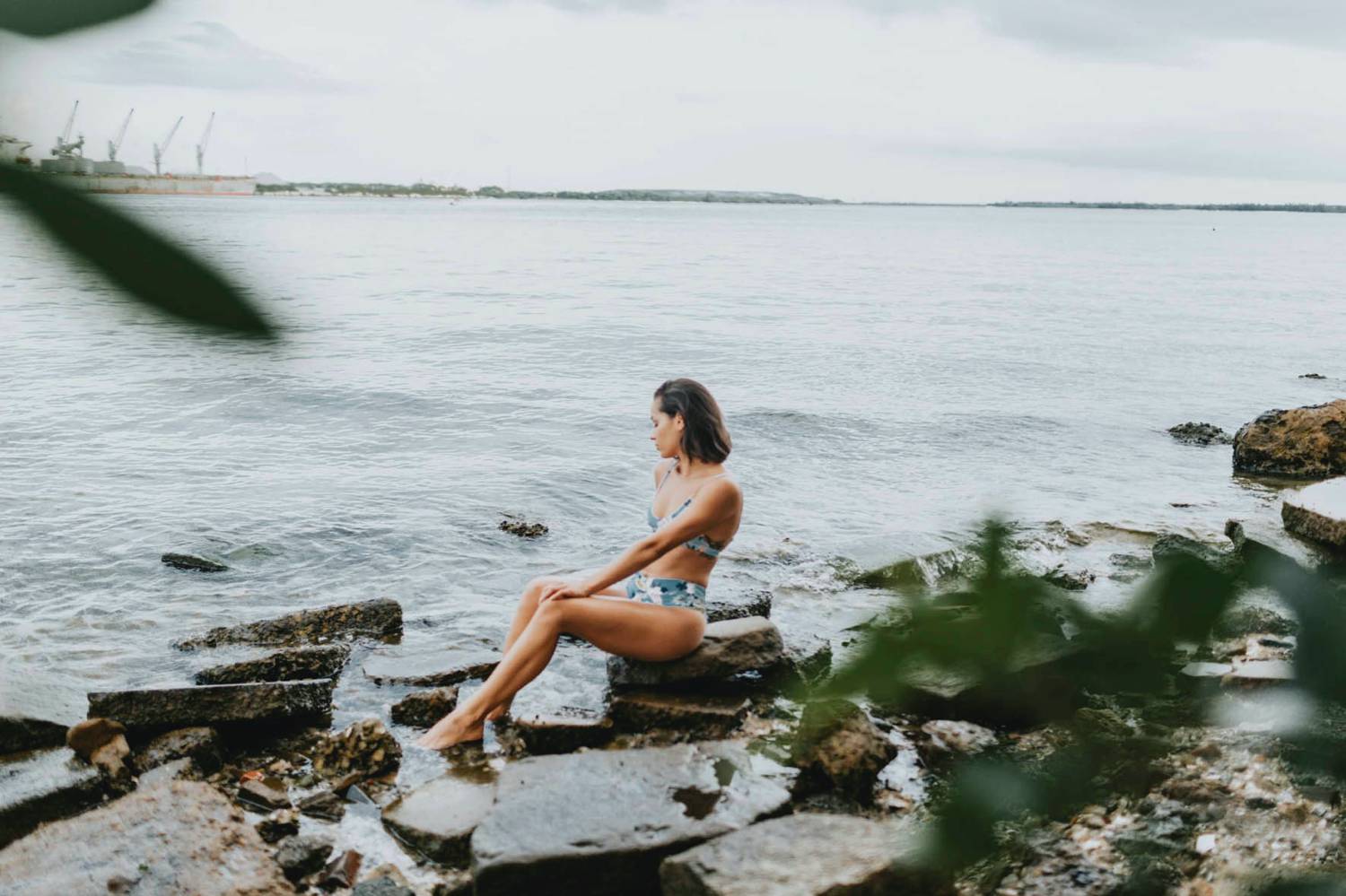 Photo: Grace Jicha's portrait of a woman in a blue bikini sitting on a rock at the edge of a lake.