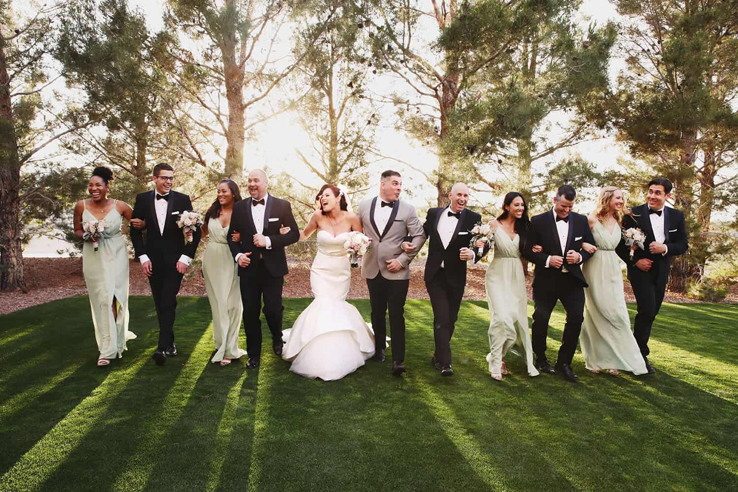 A bride and groom stroll arm-in-arm across a lawn with their bridesmaids and groomsmen.