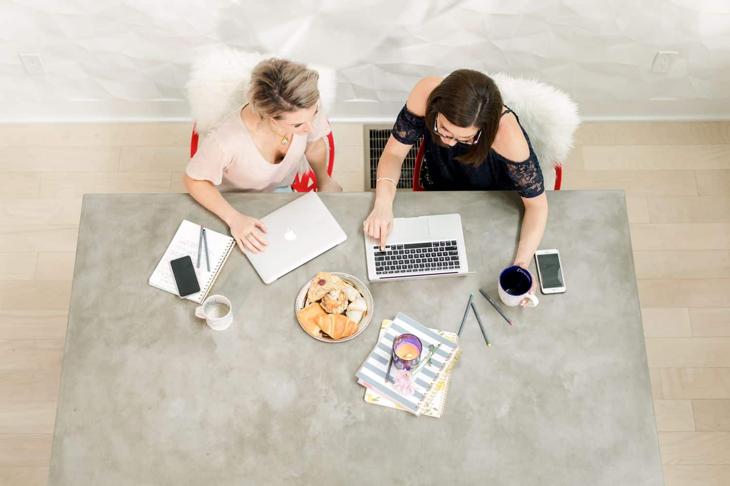 Two photographers sit at a concrete desk with their laptops and coffee.