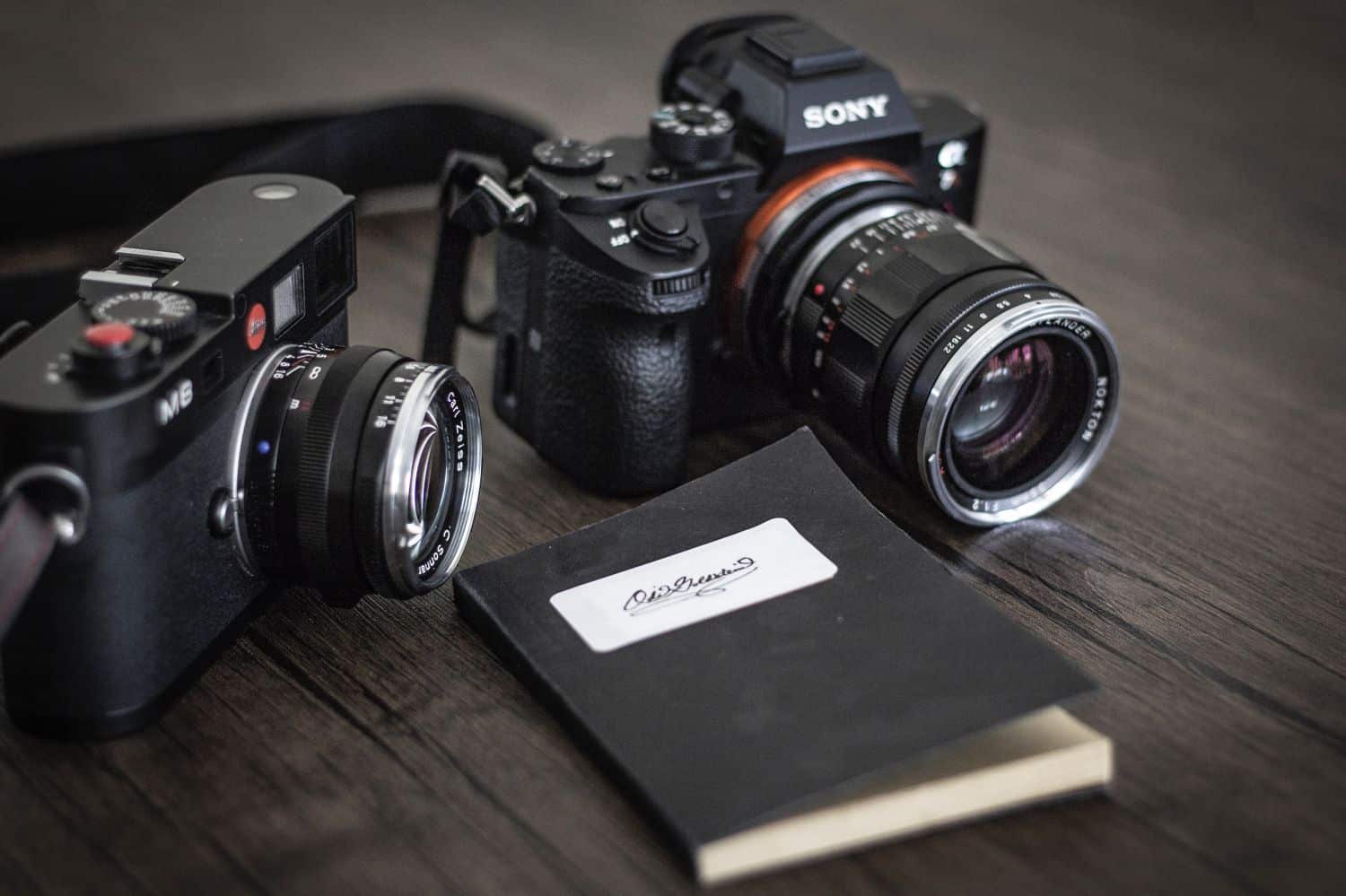 Two cameras and a black notebook placed on wooden surface
