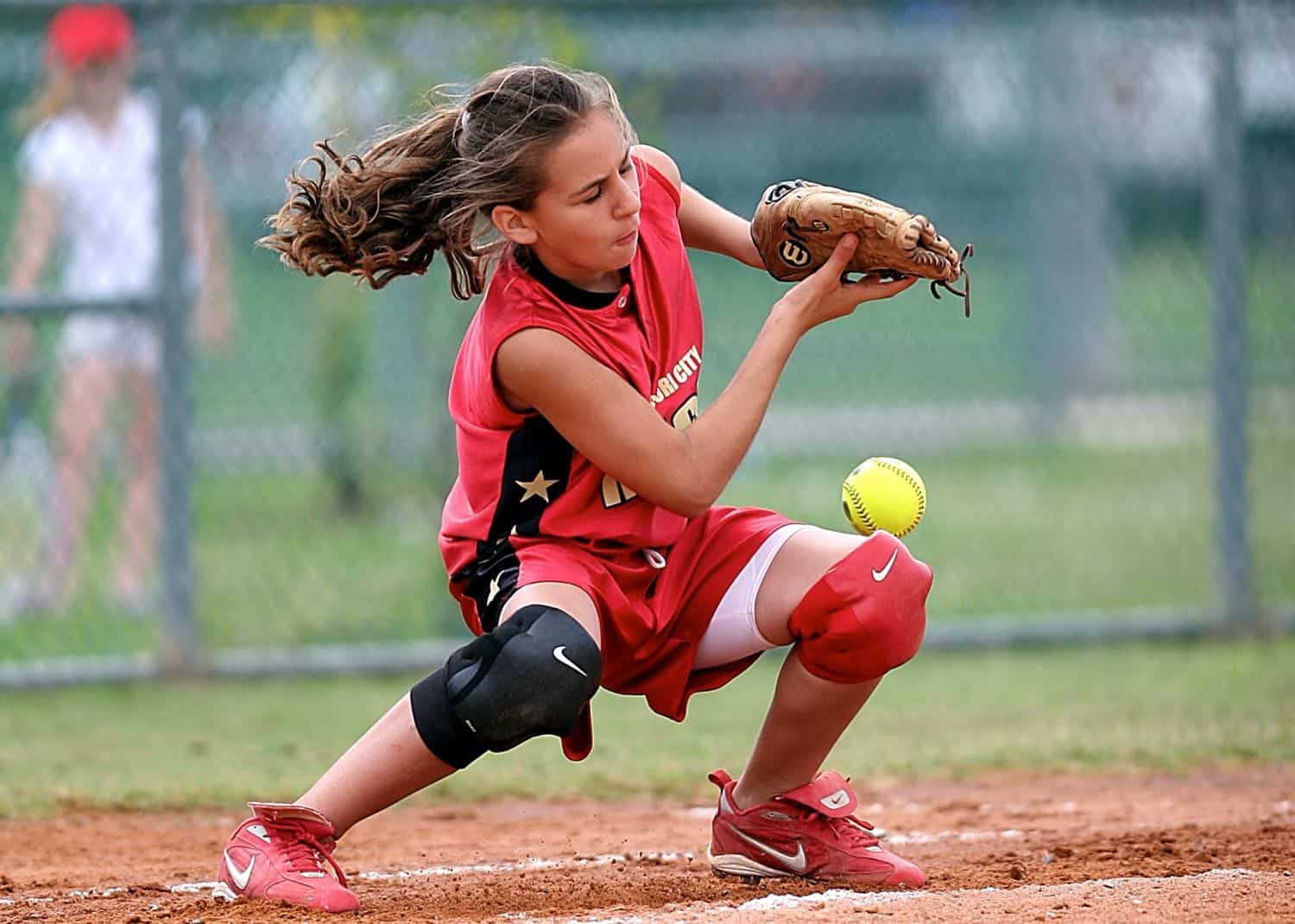 A young girl wearing a red jersey catching a softball
