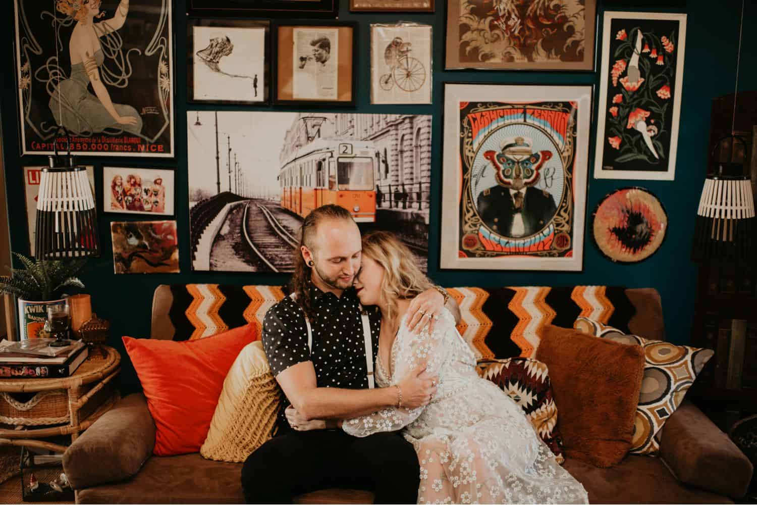 A couple embraces on their sofa. The wall behind them is covered in framed artwork. Learn how to take low light photos like Shelby Laine Photography