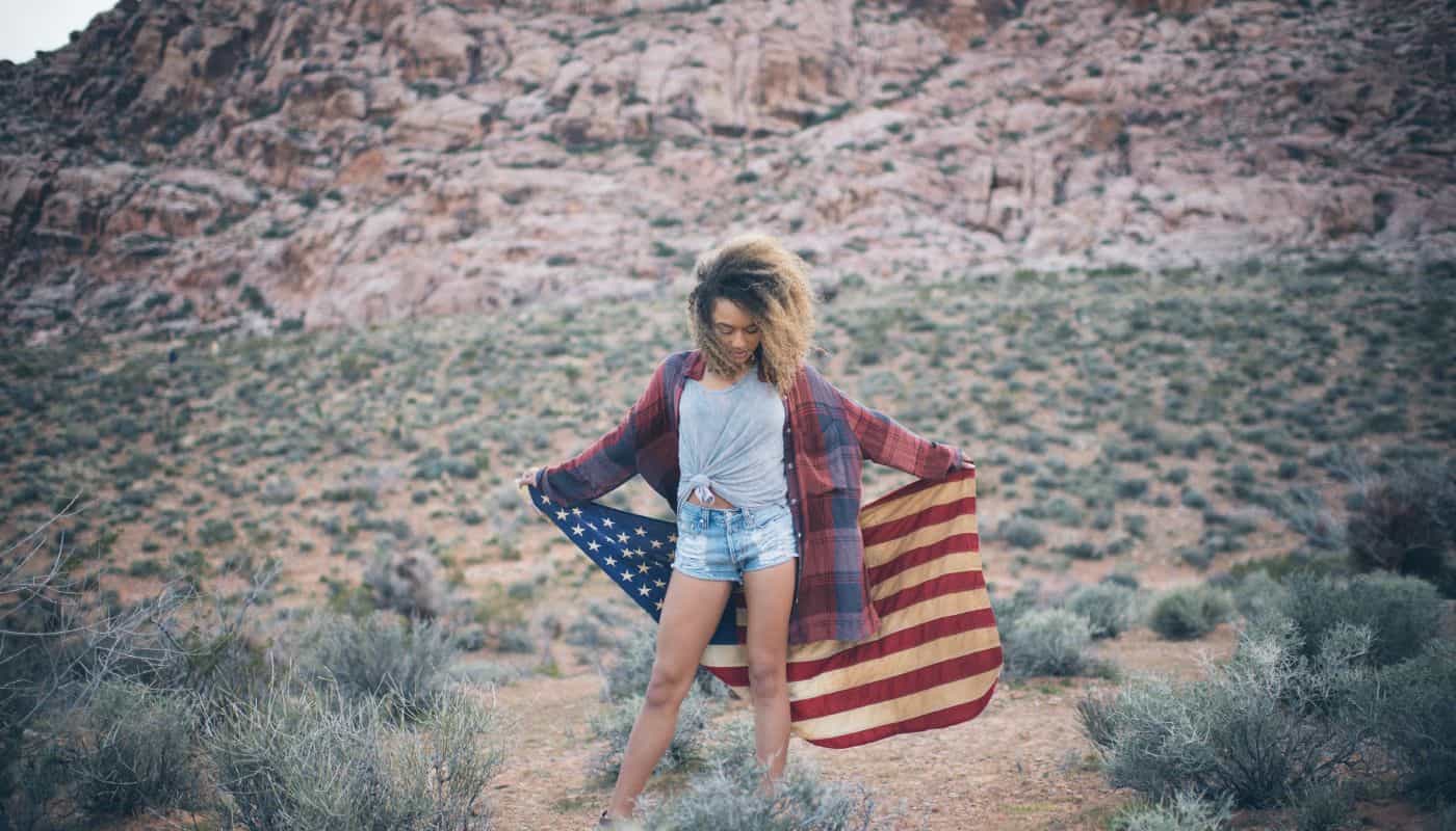 A young Black woman with natural hair holds and American flag in the desert during a digital photography session with Spanki Mills