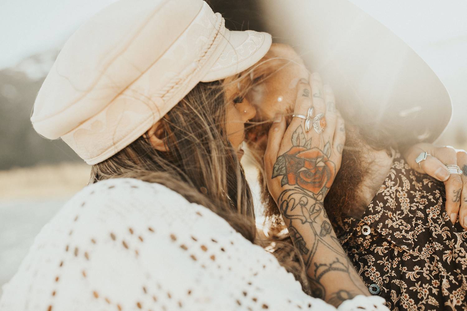 A woman in a white hat kisses a man in a black had. There is sun flare behind them.