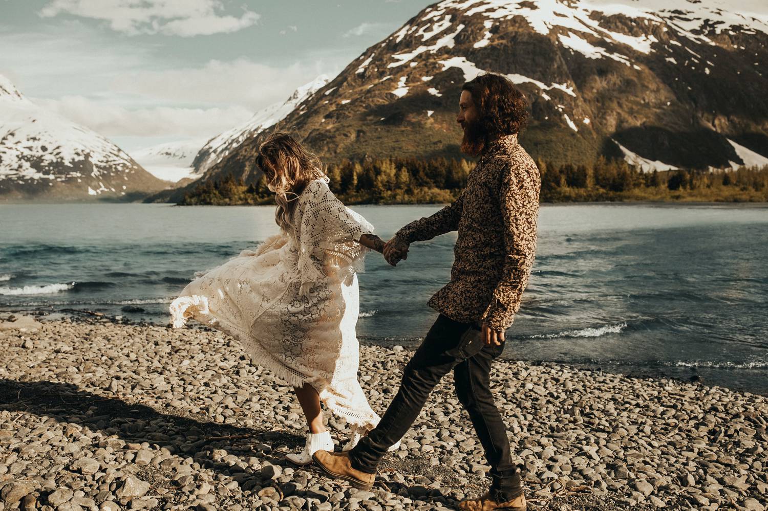 A woman wearing white walks along a rocky mountain lakeshore with a man wearing black