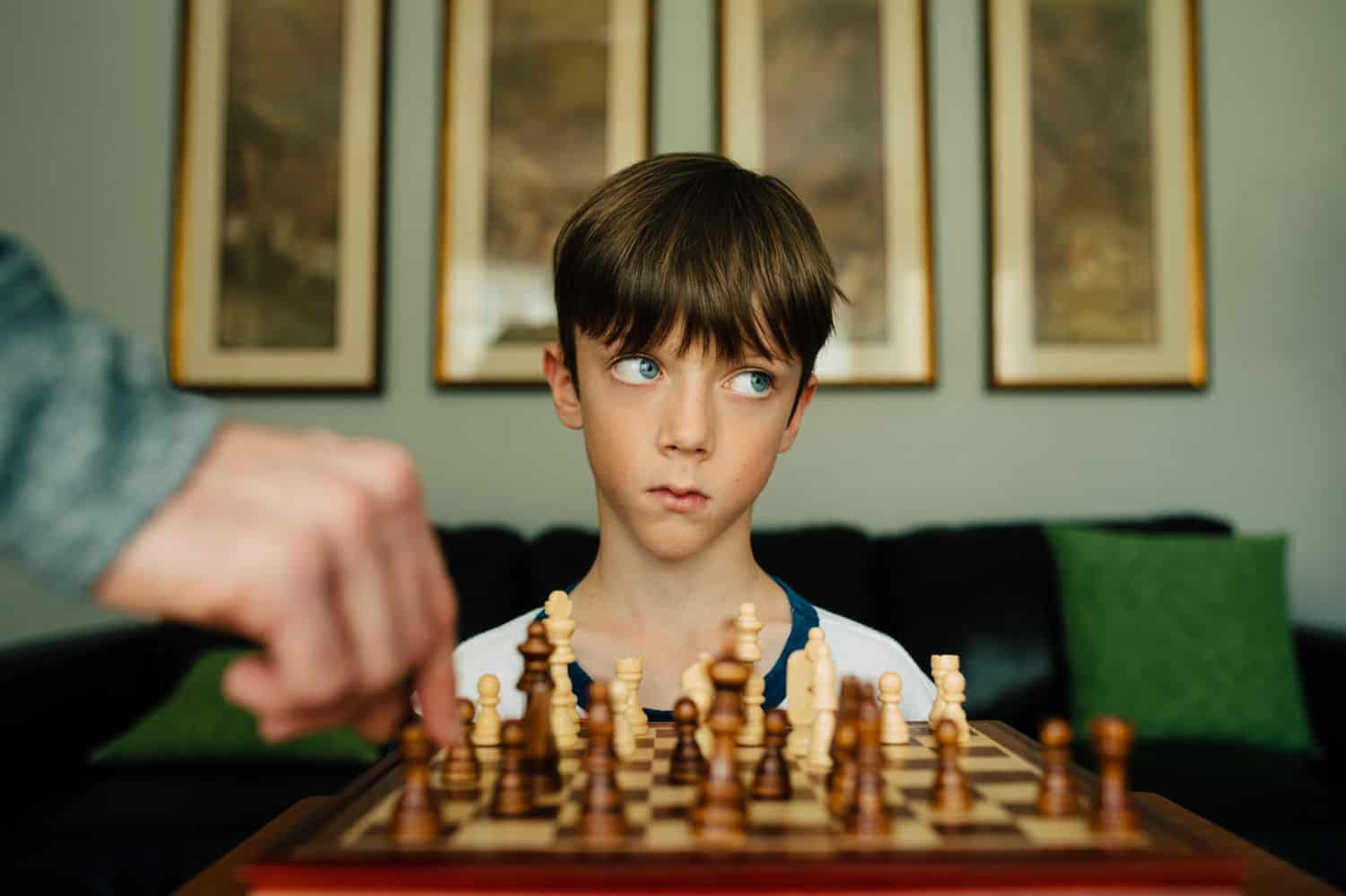 A little boy sits at a chess set rolling his eyes. By Kate T. Parker for The Heart of a Boy