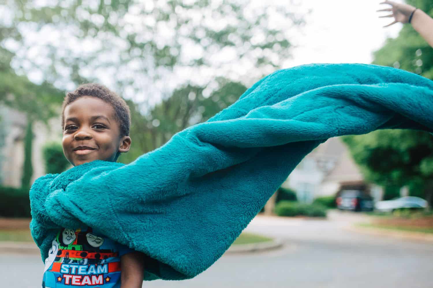 A little boy wears his blue bedspread as a cape. Photo by Kate T. Parker for The Heart of a Boy