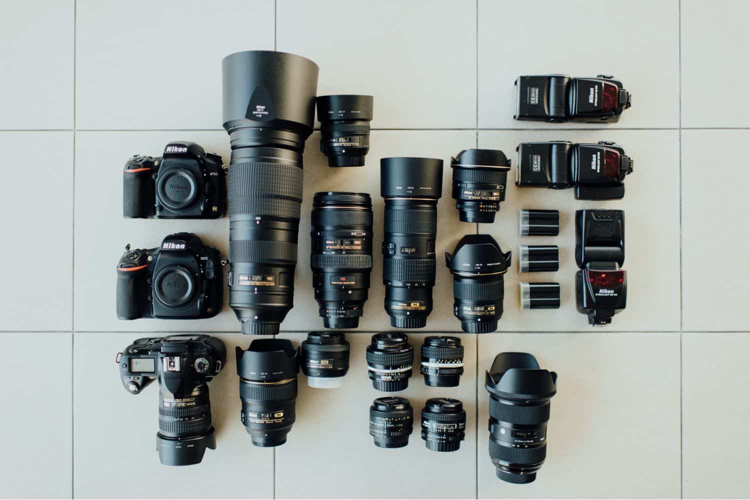 A collection of used camera lenses is laid out on a linoleum floor.