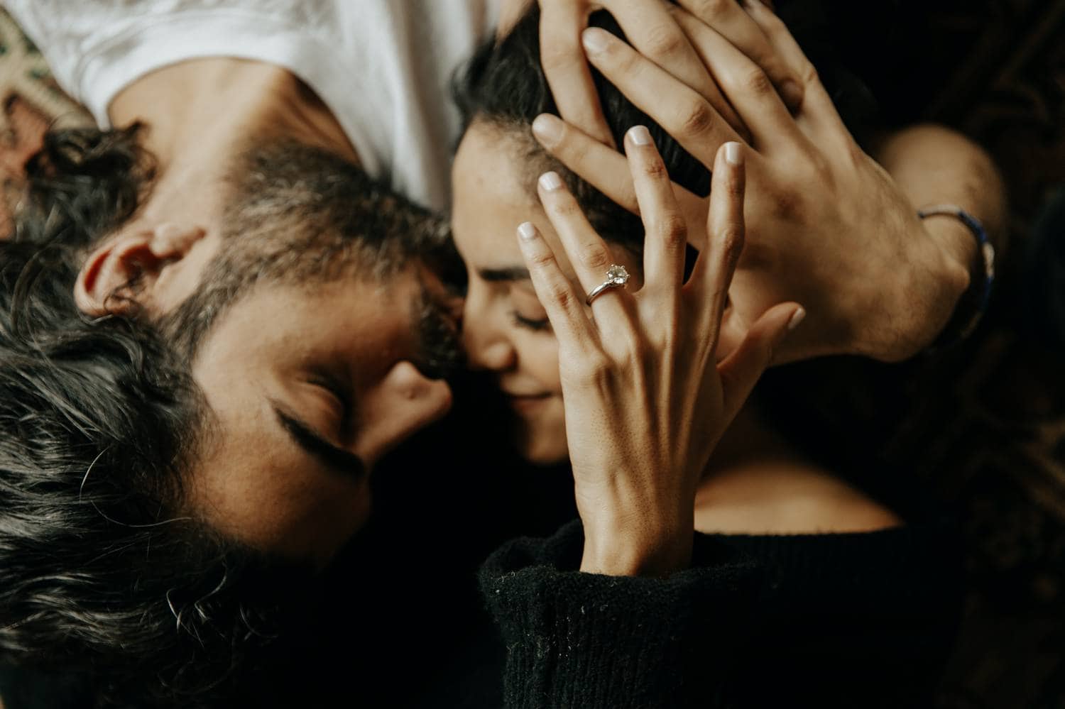 A couple lies super-close together on a bed with hands and hair intertwined. Learn how to take boudoir photos like this one from Cole's Classroom!