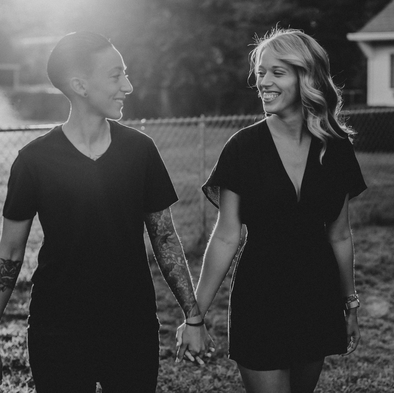 A queer couple holds hands as they stroll through their yard at dusk