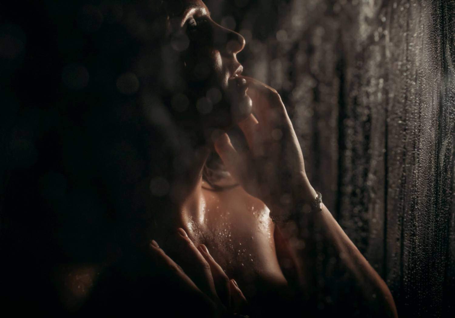 A close-up portrait shows a woman standing with eyes closed in a dim shower with the water spraying her.