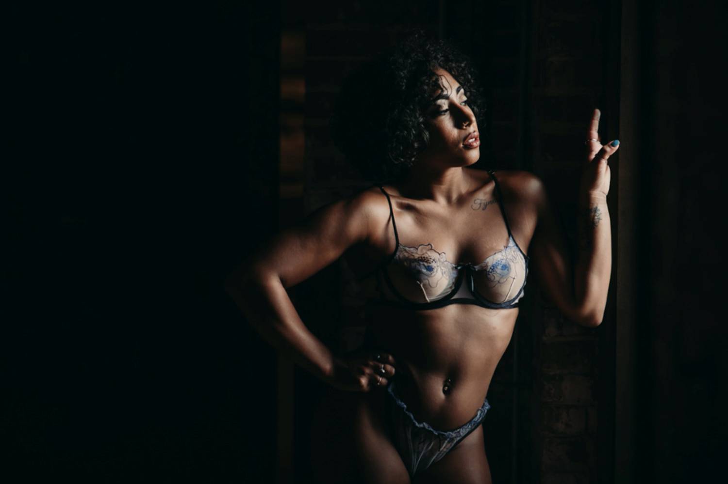 A woman in a purple bra and panties stands in window light and poses so her muscles are well-defined. Learn how to take boudoir photos like this one and more!