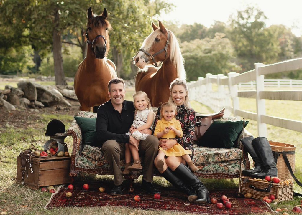 Mariah Gale Creative shoots creative family photo poses like this one, with a vintage sofa holding a smiling family as two large horses stand behind them.