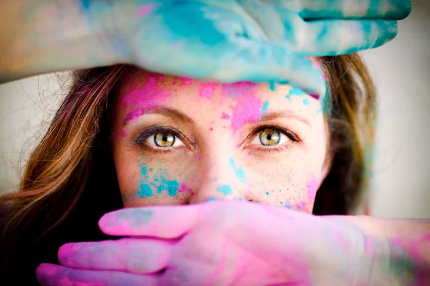 Woman's green eyes framed by paint-covered hands.