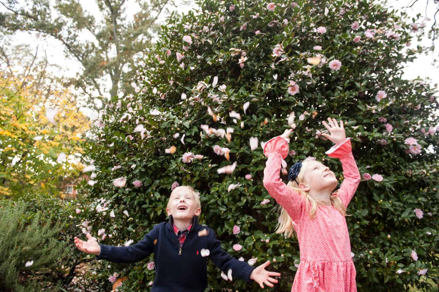 A brother and sister throw pink flower petals into the air.