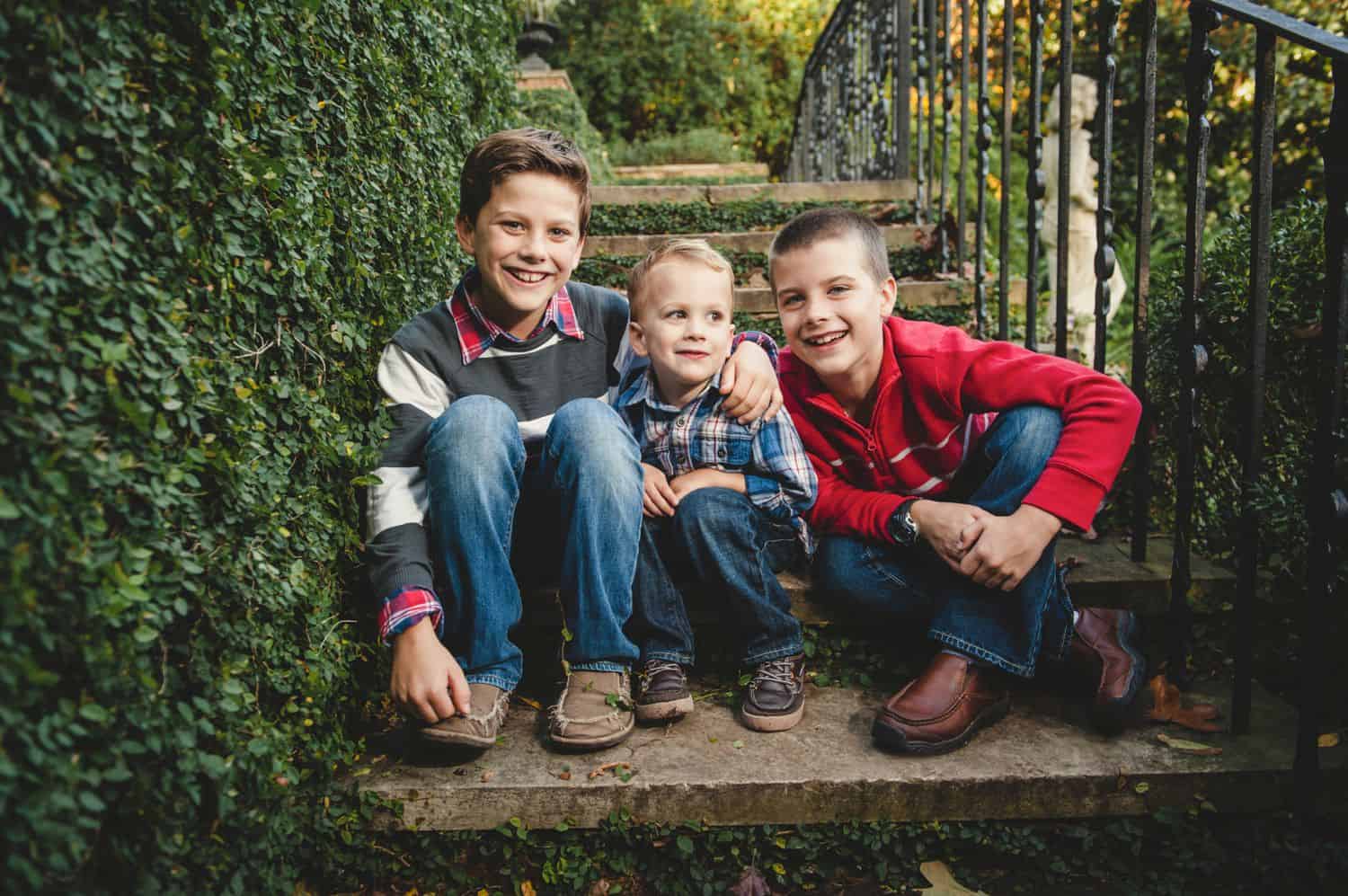 Three brothers sit together in concrete steps surrounded by ivy.