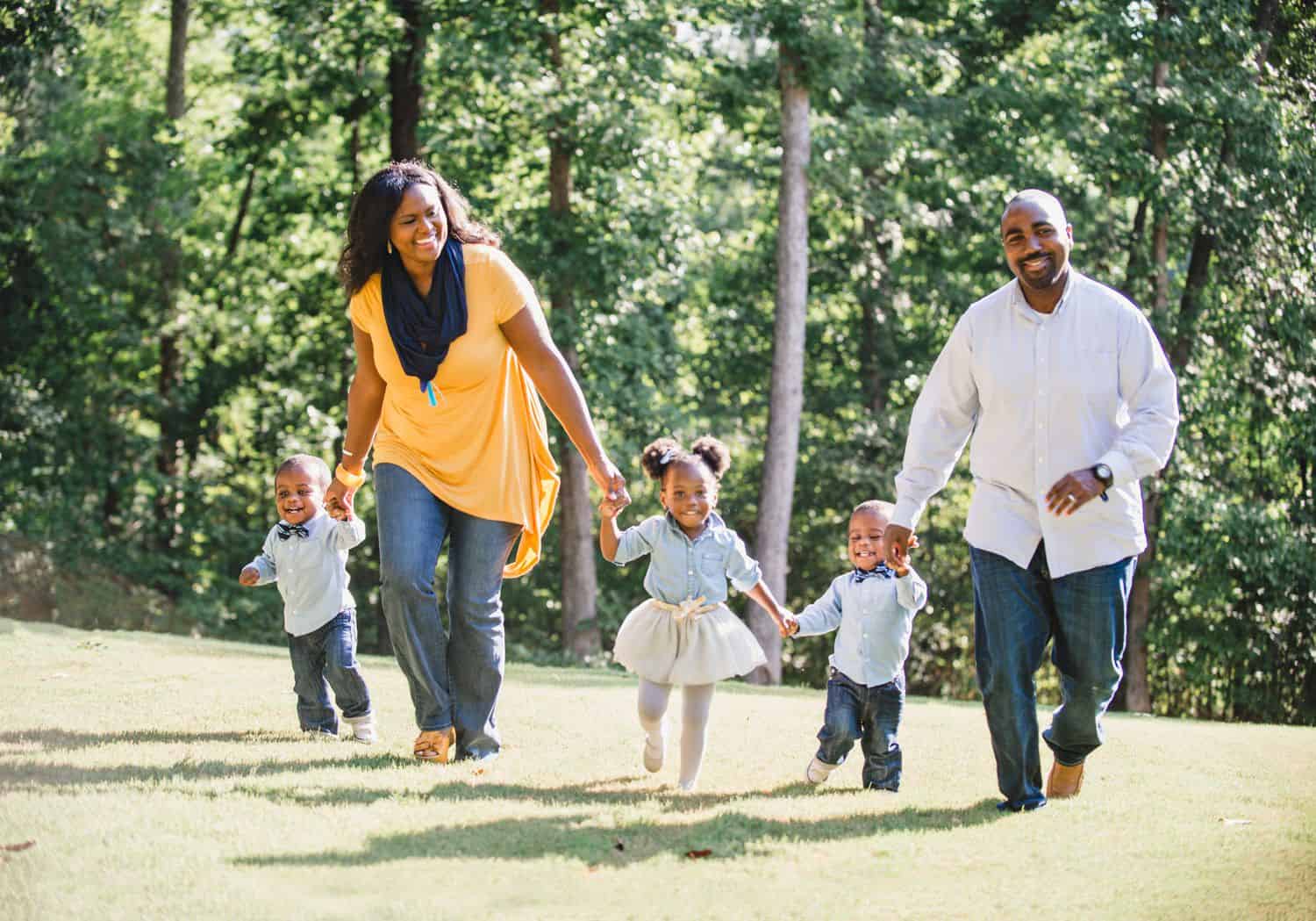 Two parents walk through a field while laughing with their three young children.