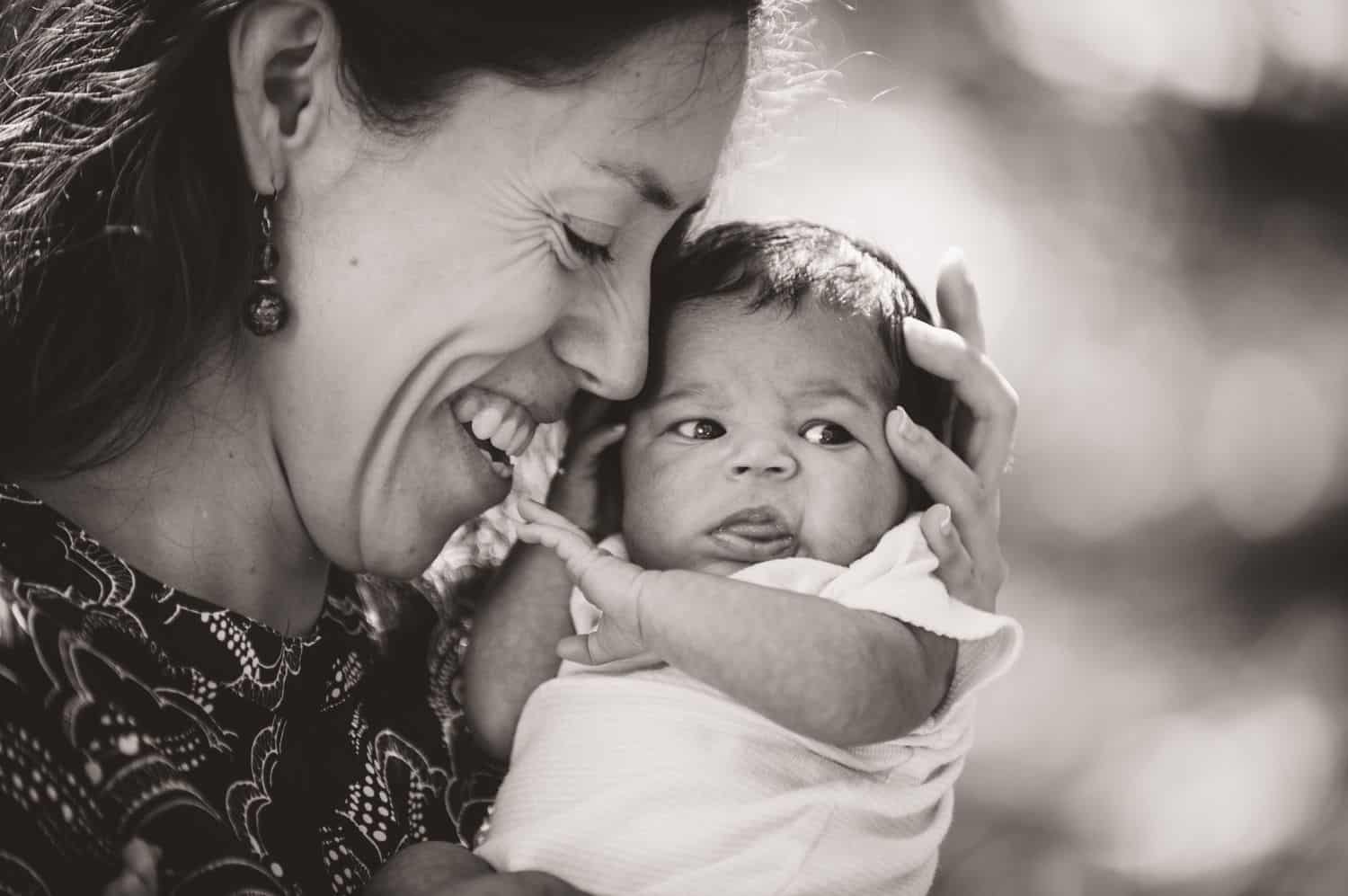 A mother snuggles her baby close to her face in black and white.