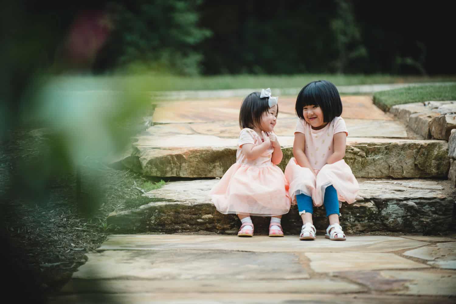 Two little girls sit on stone steps in pink dresses.