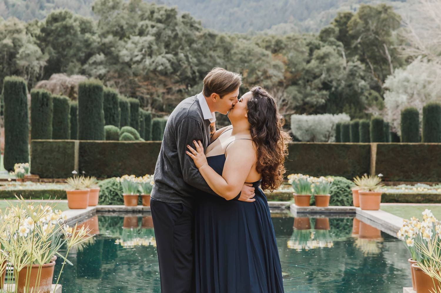 A man dips a woman for a kiss in front of a mansion's koi pond