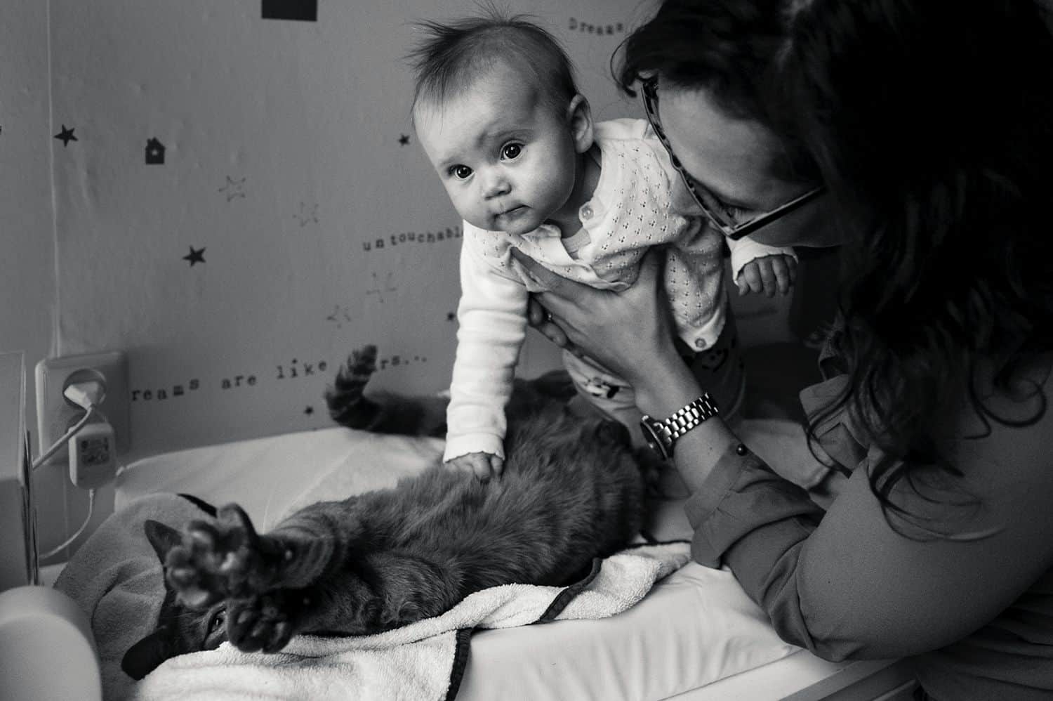A mom holds her baby over the family cat so the child can pet the animal