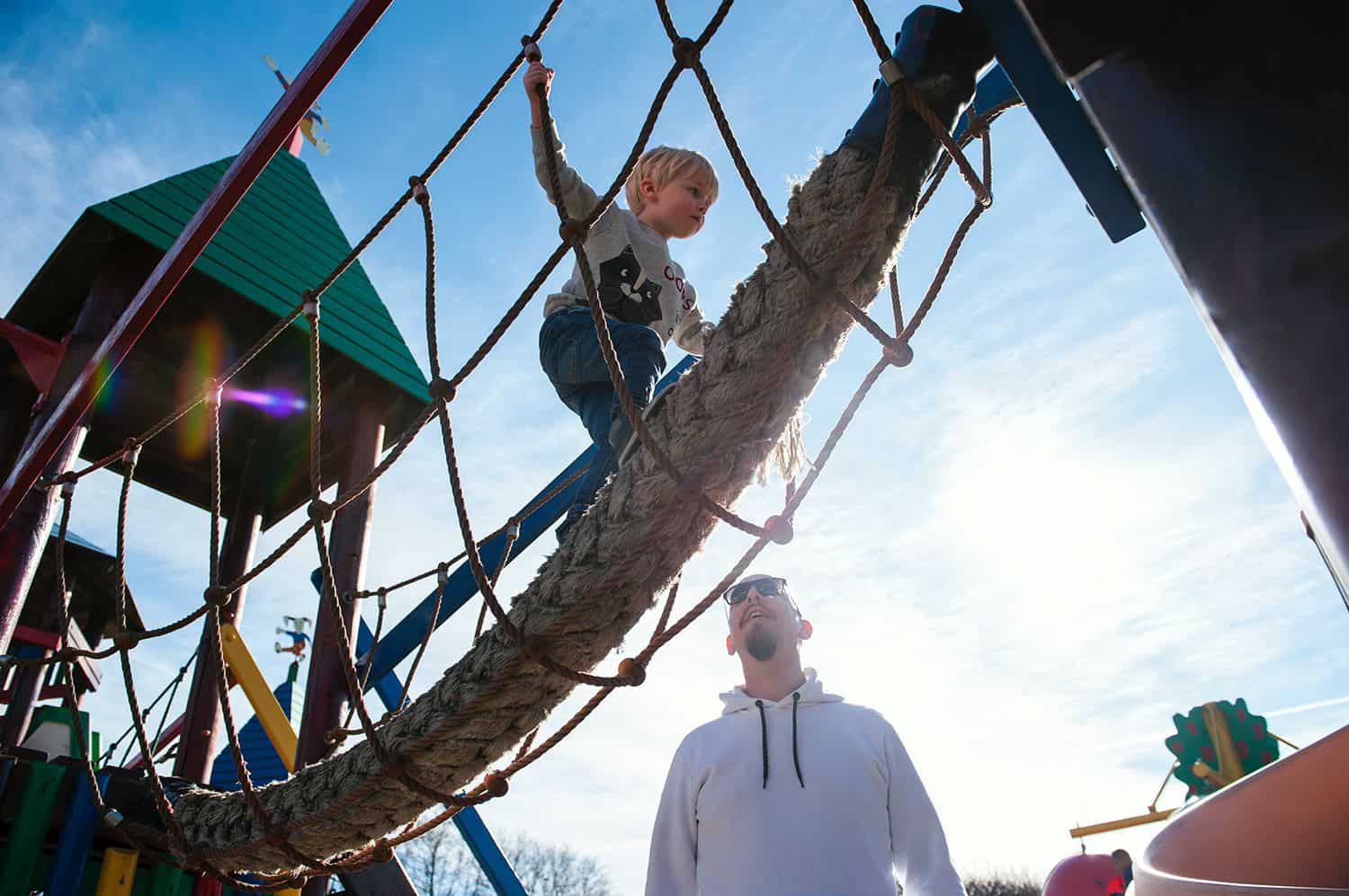 A little boy climbs across a rope bridge while his dad watched protectively from below