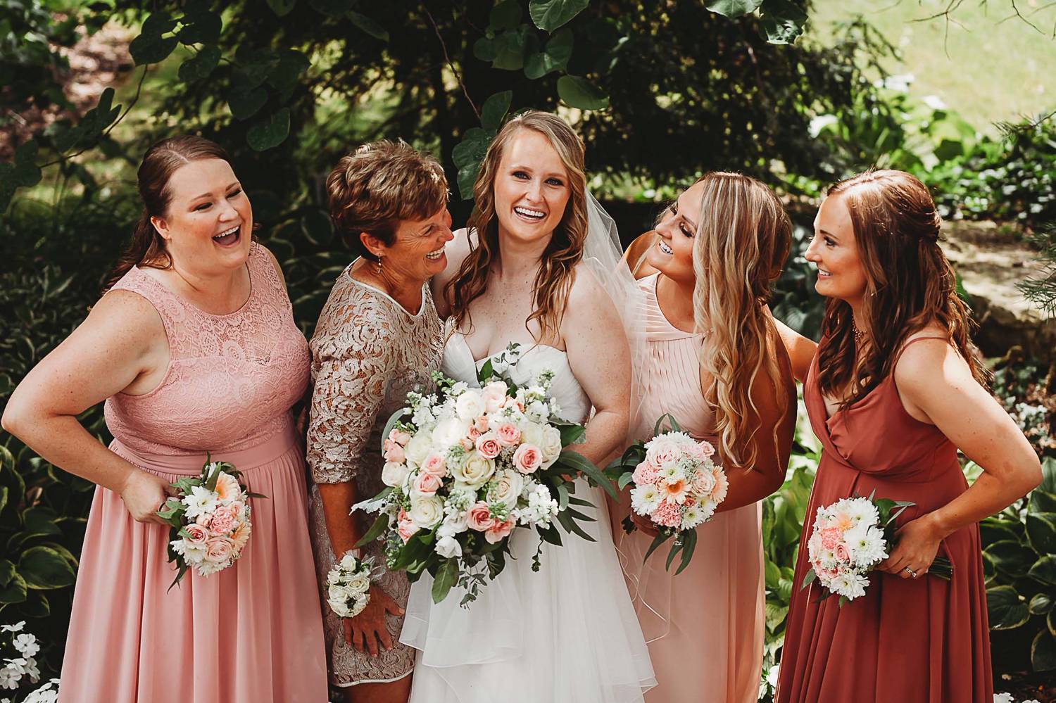 Bridesmaids in pink dresses surround a smiling bride