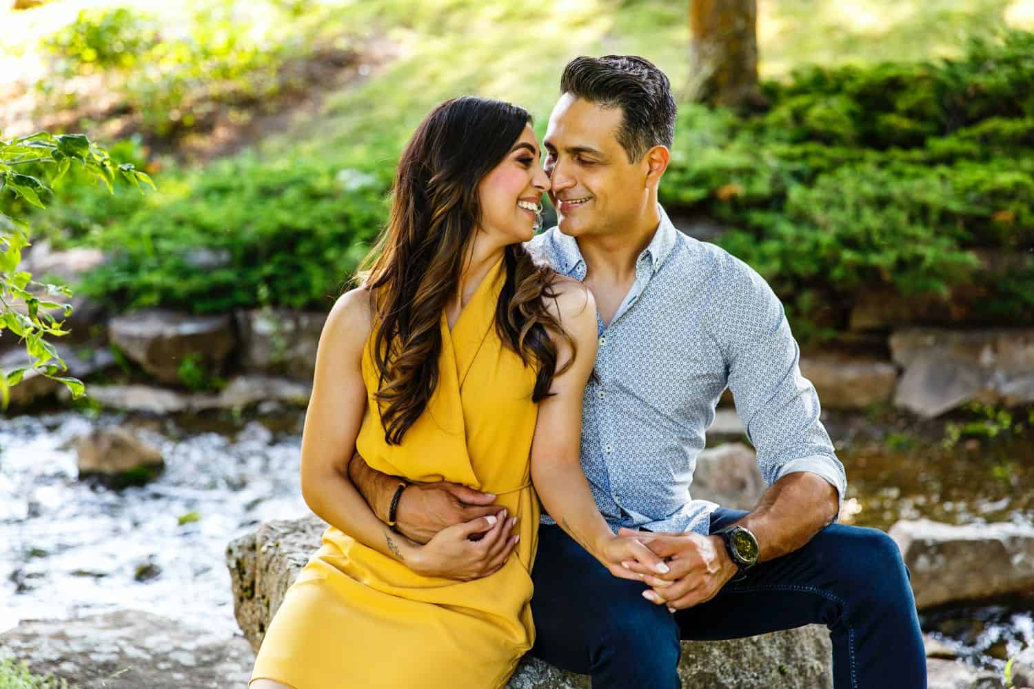 A couple holding hands and sitting down on a rock near a stream